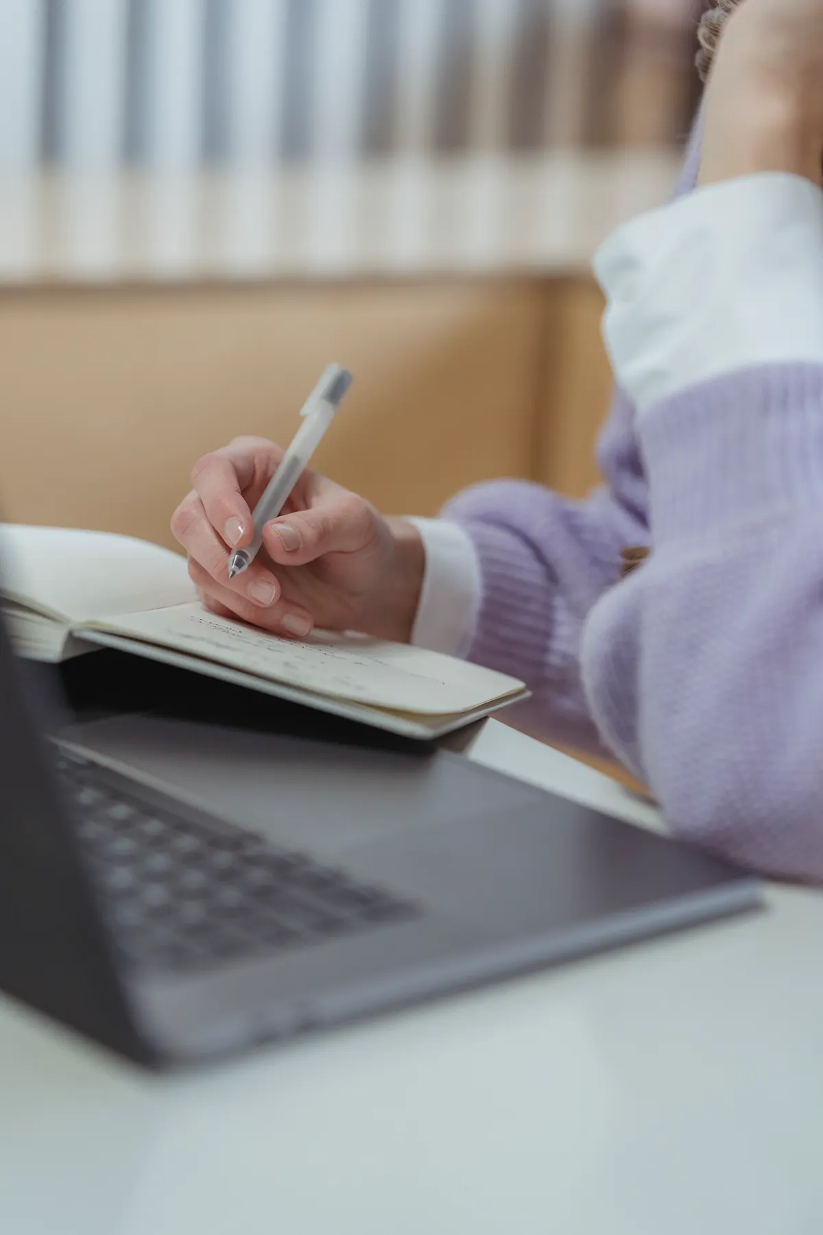 Een hand schrijft met een pen in een notitieboek boven een laptop